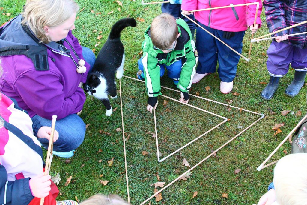 Die Drei (Erzieherin) begrüßt die Kinder und prüft: "Groß und Klein passen fein, das muss ein Dreieck sein!"
